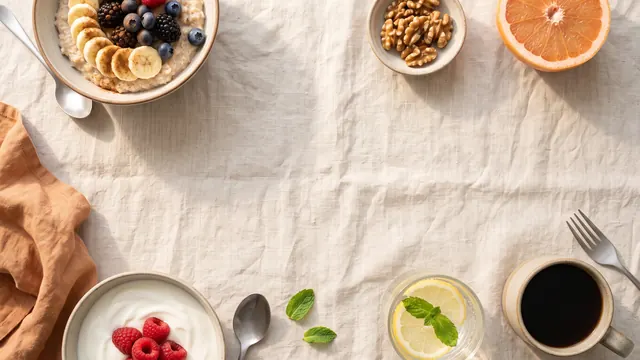 A breakfast table with oatmeal topped with fruit, yogurt with raspberries, walnuts, grapefruit, lemon water and black coffee